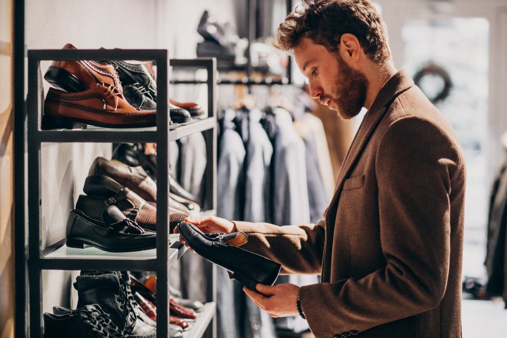 Young man in winter outfit choosing leather shoes in a stylish men’s fashion boutique in Alicante