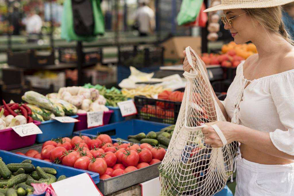 Woman shopping with net bag at vegetable stall in an open-air market in Alicante province