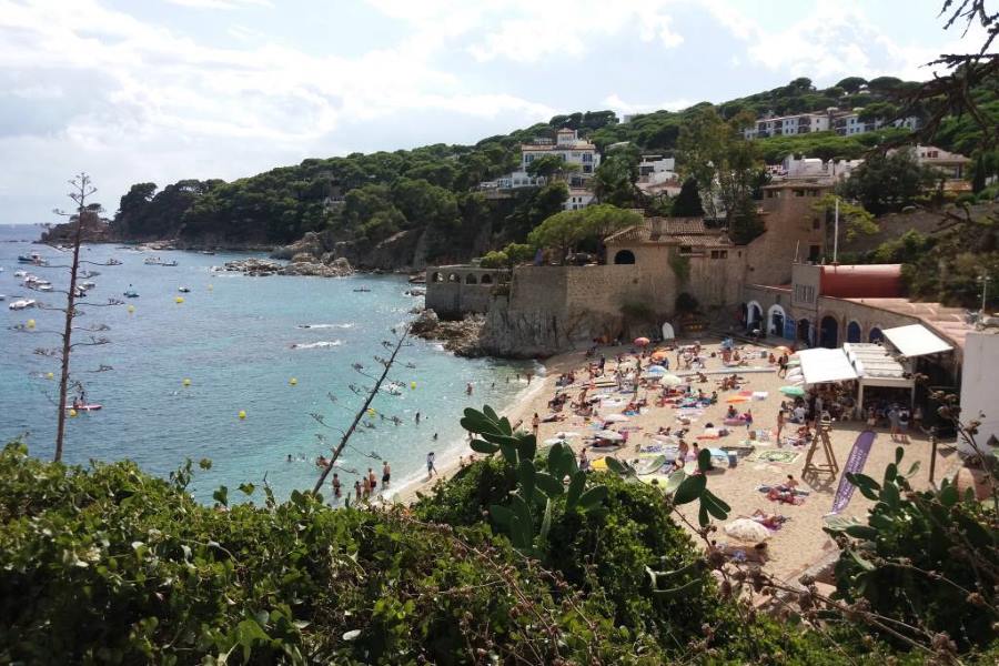 Tourists sunbathing and swimming at a small beach cove with turquoise waters on the Costa Brava