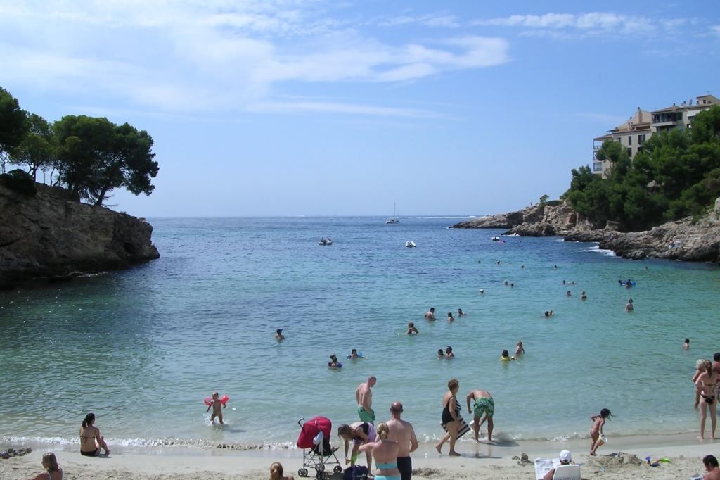 Tourists swimming in a clear water cove with rocky cliffs and pine trees in Mallorca, Balearic Islands
